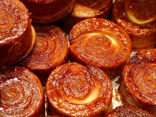 Nahaufnahme von karamellisierten Kouign Amann Gebäckstücken mit spiralförmiger Teigstruktur.