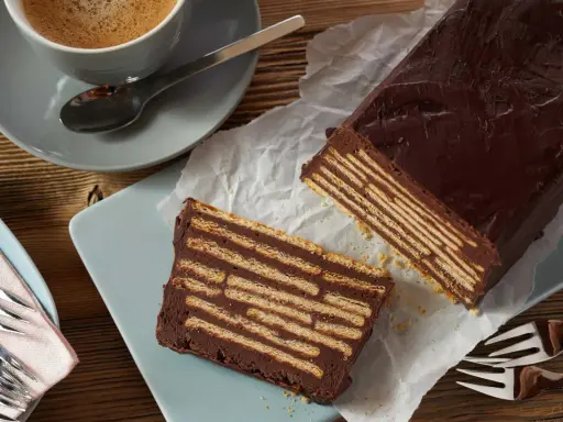 Ein Stück Schokoladenkuchen, der wie ein kalter Hund aussieht, mit Keksen und Schokoladencreme geschichtet. Daneben eine Tasse Kaffee.