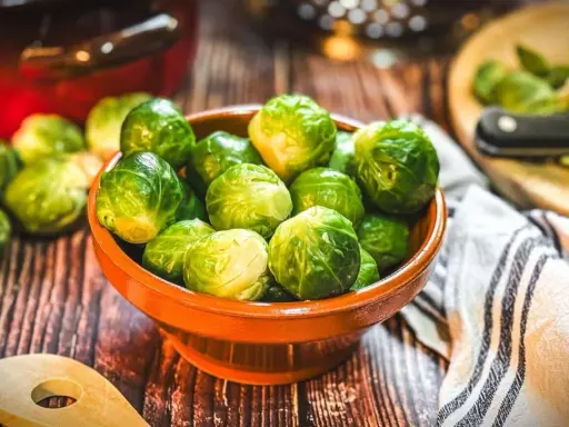 Frischer Rosenkohl in einer Schale, bereit, rosenkohl zuzubereiten wie Oma. Ein Holzlöffel liegt daneben.