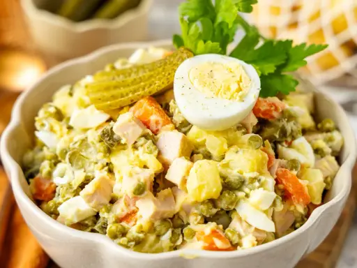 Ein cremiger Olivier Salat mit Erbsen, Karotten, Eiern und Gewürzgurken, garniert mit einer halben Eierschale und Petersilie.