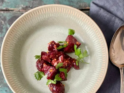 Ein köstlicher Rote Bete Feta Salat mit frischer Petersilie, serviert auf einem rustikalen Teller. Daneben liegen Löffel und Gabel.