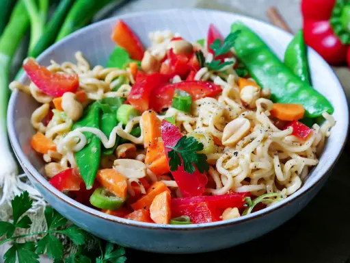 Bunter mie nudelsalat mit Erdnüssen, Paprika, Zuckerschoten und Karotten, garniert mit Petersilie.