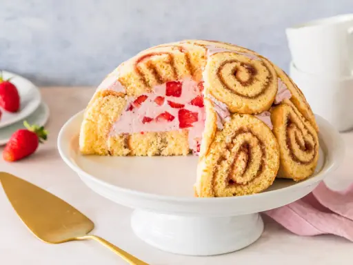 Halbierte Erdbeer Charlotte auf einer Tortenplatte, gefüllt mit Erdbeercreme und frischen Erdbeeren, umhüllt von Biskuitrollen.