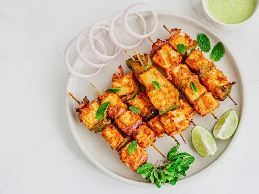 Saftiges paneer tikka auf Spießen, garniert mit Minze, Zwiebelringen und Limettenspalten.
