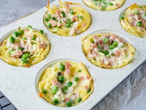 Köstliche Muffins aus nudeln vom vortag, gefüllt mit Erbsen und Schinken, überbacken mit Käse.