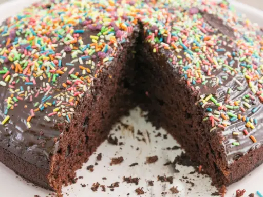 Schokoladenkuchen ohne Mehl und Ei, mit glänzender Glasur und bunten Streuseln. Ein Stück fehlt, was Lust auf mehr macht.