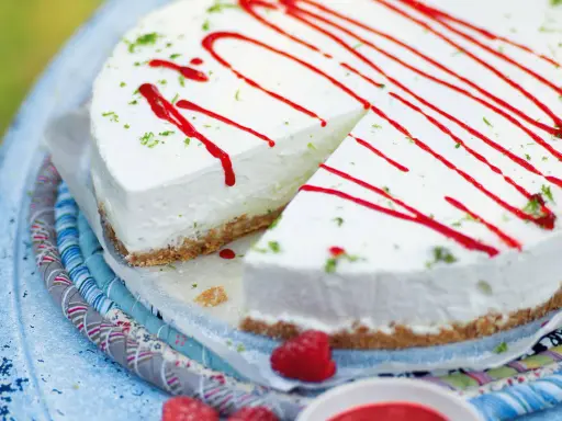 Cremiger Kuchen ohne Backen, dekoriert mit rotem Sirup und Limettenabrieb. Ein Stück ist bereits angeschnitten.