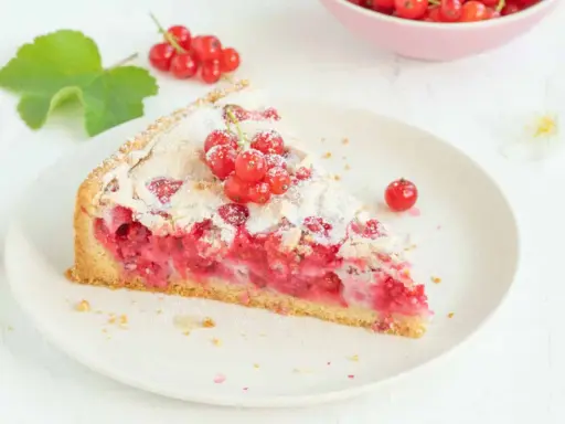 Ein Stück von Omas Johannisbeerkuchen mit Baiser, garniert mit frischen roten Johannisbeeren und Puderzucker.