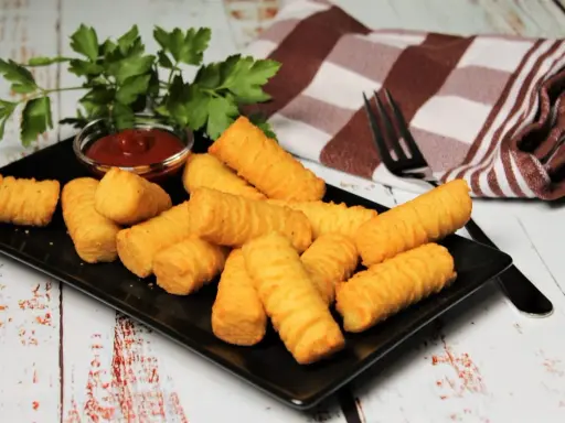 Goldbraune Kroketten, frisch zubereitet, liegen auf einem schwarzen Teller. Dazu gibt es Ketchup und frische Petersilie. Perfekt zum selber machen!