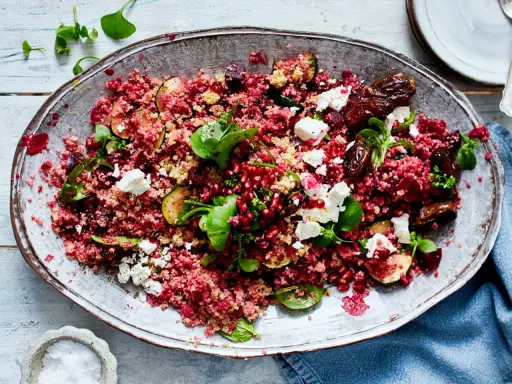 Rote Bete Bulgur Salat mit Granatapfelkernen, Feigen, Feta und frischen Kräutern auf einem ovalen Teller.
