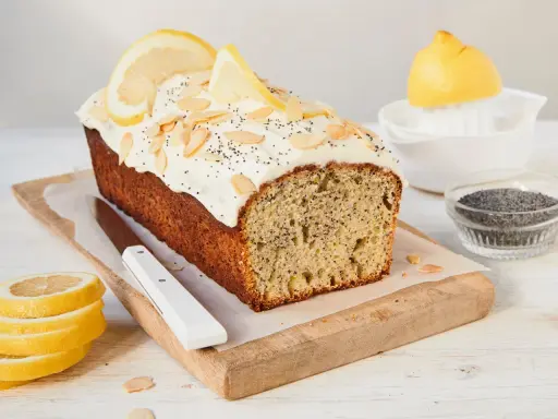 Saftiger zitronen mohn kuchen mit weißem Zuckerguss, Mandelsplittern und Mohn bestreut. Zitronenscheiben zieren die Oberseite.