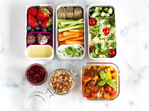 Vorbereitete Mahlzeiten für das meal prep einfrieren: Obst, Gemüse-Sticks, Hummus, Couscous-Salat und Linseneintopf.