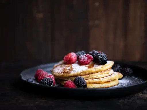 Ein Stapel fluffiger Pancakes, garniert mit frischen Beeren und Puderzucker. Ein perfektes pancakes rezept fluffig für jeden Anlass.