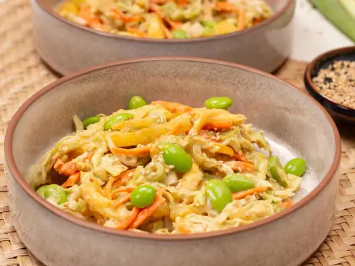 Ein cremiger asiatischer Salat mit knackigem Kohl, Karottenstreifen und Edamame, garniert mit Sesam.
