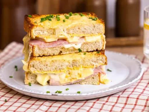 Ein gestapelter Croque Monsieur mit geschmolzenem Käse, Schinken und Schnittlauch auf einem Teller.