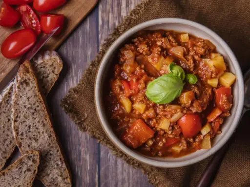 Herzhaftes Bauerntopf Rezept: Hackfleisch, Kartoffeln und Tomaten in einer Schüssel, garniert mit Basilikum. Dazu gibt es rustikales Brot.