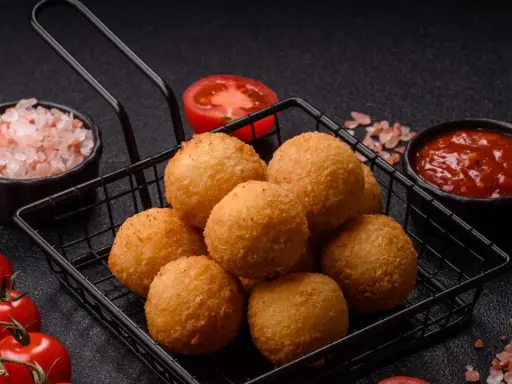 Goldbraune Arancini im Korb, bereit für ein köstliches arancini rezept. Dazu frische Tomaten, Salz und Dip.