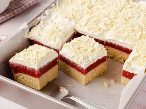 Schneeweiße Sahne und rote Fruchtschicht auf hellem Boden, bestreut mit weißer Schokolade. Ein köstlicher Frau Holle Kuchen, der zum Reinbeißen einlädt.