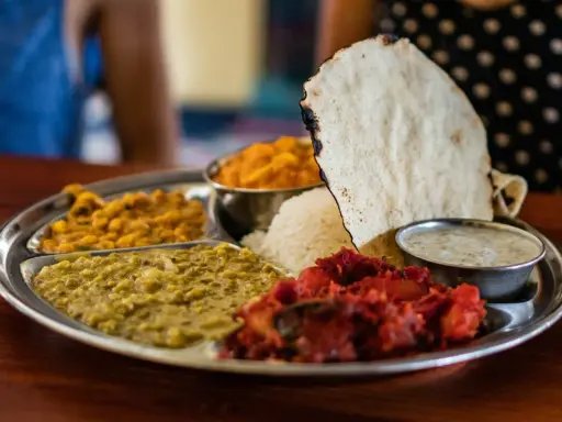 Vielfalt an indischen Gerichten auf einer Thali-Platte: Reis, Linsen, Curry und Papadum.