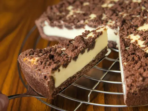 Ein Stück russischer Zupfkuchen wird aus dem Ganzen gehoben. Der Kuchen hat einen dunklen Boden, eine helle Füllung und eine krümelige Schokoladenstreusel-Decke.