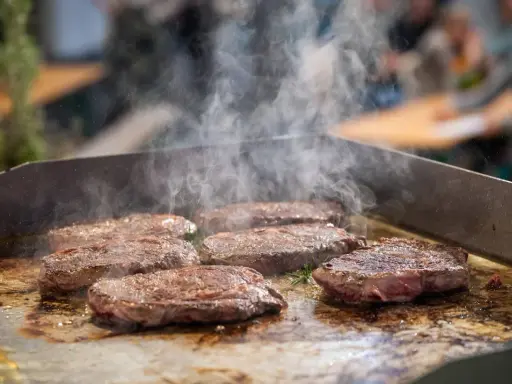 Mehrere saftige Steaks brutzeln auf einer heißen Platte. Dampf steigt auf und zeigt, wie man ein Steak richtig braten kann.