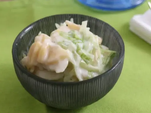 Ein cremiger Kartoffelsalat mit Joghurt und knackigem Gemüse, serviert in einer dunklen Schüssel auf einem hellgrünen Tischtuch.