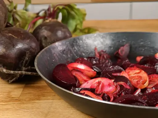 Rote Bete wird in einer Pfanne zubereitet, ein köstliches Hauptgericht. Frische Rote Bete liegt daneben.