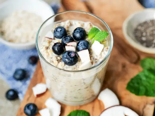 Ein Glas cremiger Overnight Oats mit Blaubeeren, Kokosnuss und Minze. Perfekt für ein schnelles Frühstück.