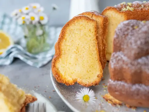Saftiger Omas Joghurt Kuchen, mit Puderzucker bestäubt und Zitronenschale garniert. Ein Stück davon liegt auf einer Gabel.