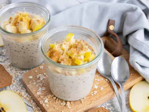 Zwei Gläser mit Overnight Oats Grundrezept, garniert mit Apfelstücken und Zimt. Perfekt für ein schnelles Frühstück.