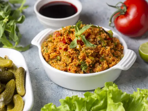 Ein köstliches Kisir-Rezept mit Bulgur, Tomaten und Kräutern, garniert mit Minze. Daneben Cornichons, Granatapfelsirup, Limette und ein frischer Kopfsalat.