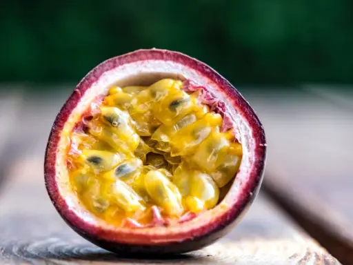Eine aufgeschnittene Passionsfrucht mit saftigem, gelbem Fruchtfleisch und schwarzen Kernen liegt auf Holzplanken. Ein Genuss, diese Passionsfrucht zu essen!
