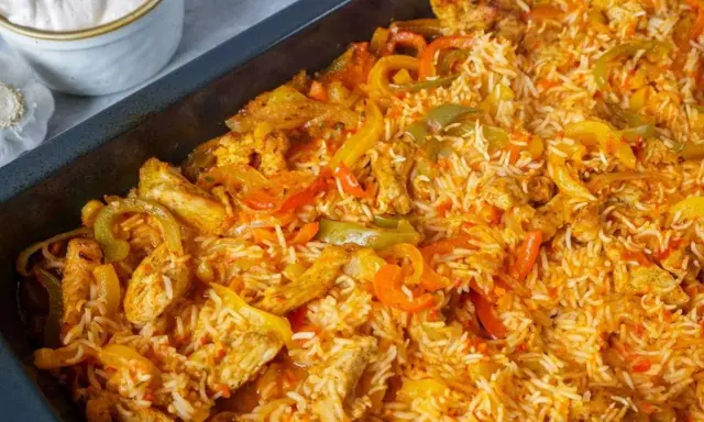 Herzhaftes One Pot Reis Ofen Gericht mit Hähnchenstreifen und bunten Paprikastreifen, serviert in einer schwarzen Auflaufform.