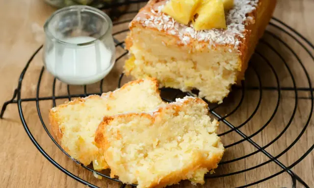 Saftiger ananas kokos kuchen mit frischer Ananas und Kokosraspeln, serviert auf einem Gitter mit einem Glas Milch.