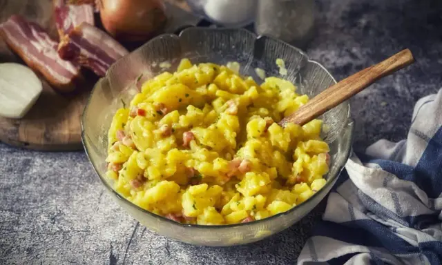 Schüssel mit warmem Kartoffelsalat, garniert mit Speck und Zwiebeln, bereit zum Servieren.