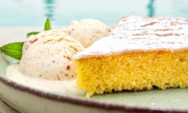 Ein Stück mallorquinischer Mandelkuchen mit zwei Kugeln Eis und Minze, serviert auf einem Teller am Pool.