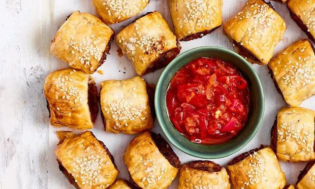 Goldbraune Würstchenschnecken mit Sesam, daneben eine Schale mit roter Chutney-Sauce. Perfekt, um schnelles Fingerfood am Vortag zuzubereiten.