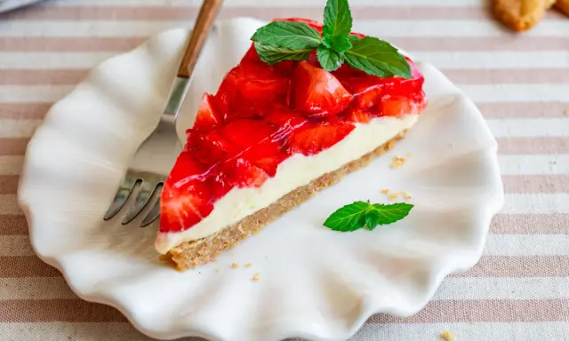 Ein Stück Erdbeerkuchen mit einer cremigen Füllung und glänzender Erdbeerschicht, garniert mit Minze. Diese torte ohne sahne ist ein Genuss.