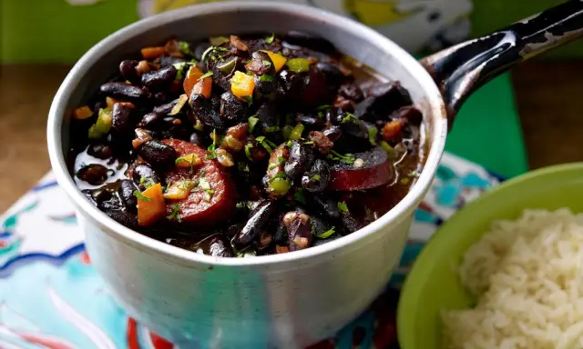 Herzhaftes schwarze bohnen rezept im Topf, mit Wurst und Gemüse, daneben eine Schüssel Reis.