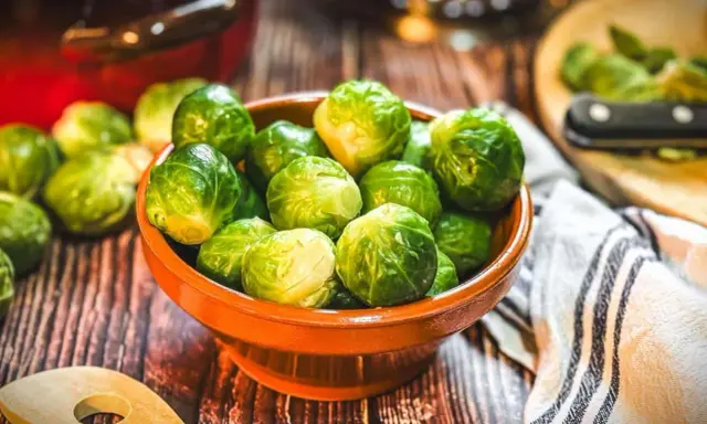Frischer Rosenkohl in einer Schale, bereit, rosenkohl zuzubereiten wie Oma. Ein Holzlöffel liegt daneben.