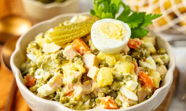 Ein cremiger Olivier Salat mit Erbsen, Karotten, Eiern und Gewürzgurken, garniert mit einer halben Eierschale und Petersilie.