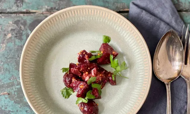 Ein köstlicher Rote Bete Feta Salat mit frischer Petersilie, serviert auf einem rustikalen Teller. Daneben liegen Löffel und Gabel.