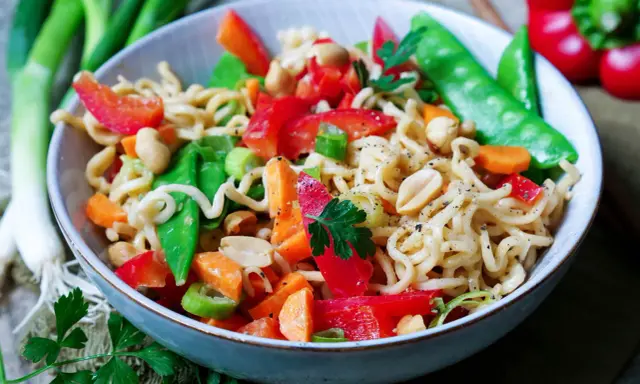 Bunter mie nudelsalat mit Erdnüssen, Paprika, Zuckerschoten und Karotten, garniert mit Petersilie.