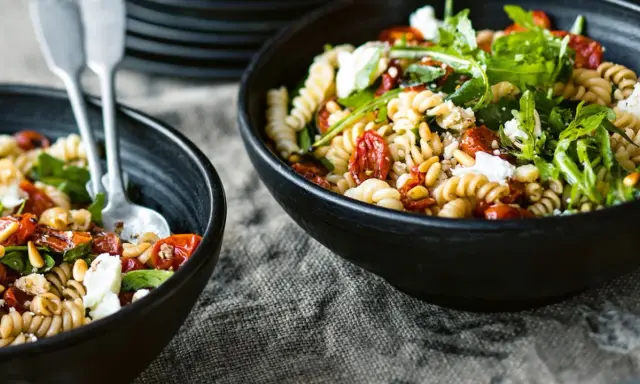 Zwei Schalen mit einem köstlichen nudelsalat mit getrockneten tomaten, garniert mit Rucola und Pinienkernen.