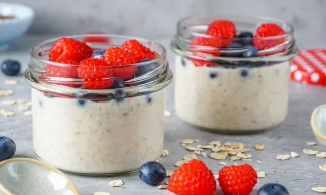 Zwei Gläser mit Overnight Oats, garniert mit frischen Himbeeren und Blaubeeren. Perfekt für ein leckeres, low carb Frühstück.