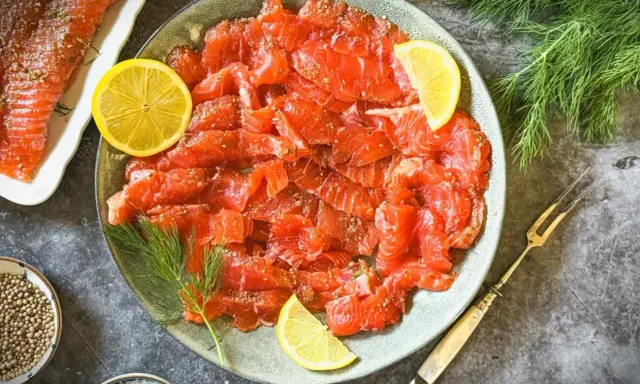 Frisch gebeizter Lachs auf einem Teller, garniert mit Zitronenscheiben und Dill. Daneben eine Schale mit Koriandersamen.