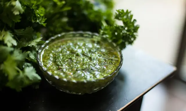 Frische Kräuter umgeben eine Schale mit leuchtend grünem Chimichurri. Was ist Chimichurri? Eine würzige argentinische Sauce aus Petersilie, Knoblauch und Essig.