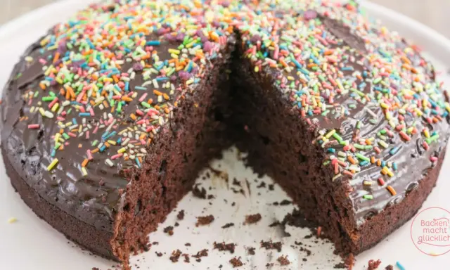 Schokoladenkuchen ohne Mehl und Ei, mit glänzender Glasur und bunten Streuseln. Ein Stück fehlt, was Lust auf mehr macht.