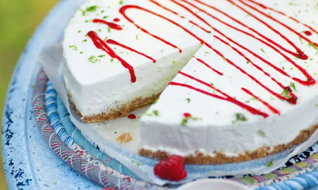 Cremiger Kuchen ohne Backen, dekoriert mit rotem Sirup und Limettenabrieb. Ein Stück ist bereits angeschnitten.