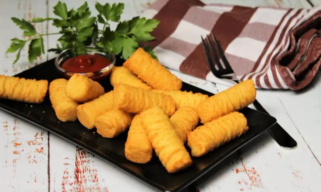 Goldbraune Kroketten, frisch zubereitet, liegen auf einem schwarzen Teller. Dazu gibt es Ketchup und frische Petersilie. Perfekt zum selber machen!